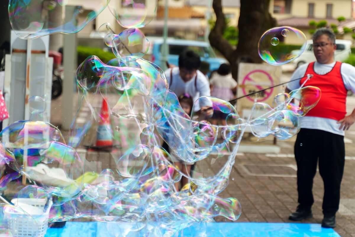 巨大シャボン玉をつくるスタッフとそれを見守る親子
